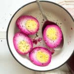 Four halved pickled eggs sprinkled with black pepper in a pot.