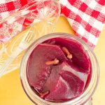 A top view of a jar filled with glossy, pickled beet slices and whole cloves.