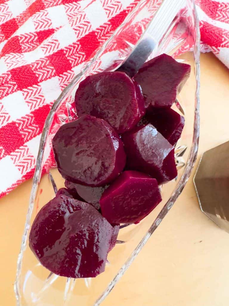 Slices of pickled beets in a clear glass dish with a serving fork.