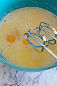 Two raw eggs in a blue mixing bowl with a hand mixer ready to blend the ingredients.