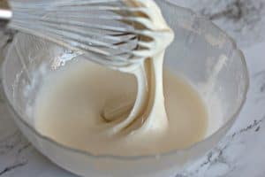 Whisk lifting smooth glaze from a bowl.