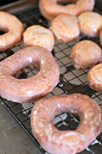 Freshly glazed Amish Doughnuts on a wire rack.