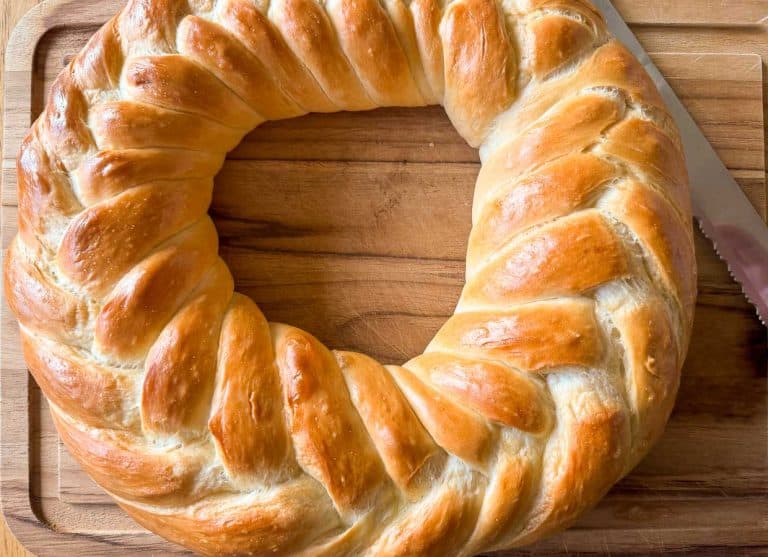Golden-brown braided bread wreath on a wooden board with a knife beside it.