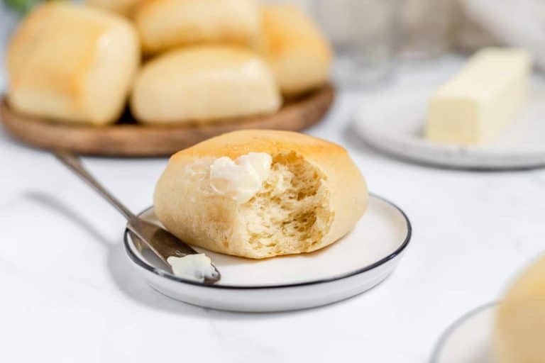 A soft, buttery Texas Roadhouse roll on a plate with more rolls in the background.
