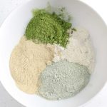 Bowl with four types of powders for green tea cleansing grains: brown rice, matcha powder, bentonite clay, and lemon peel powder.