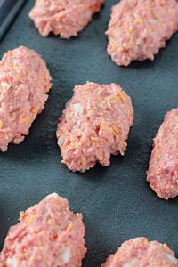 Unbaked mini meatloaves arranged on a baking sheet.