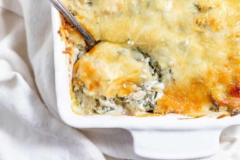 Spinach artichoke chicken casserole with melted cheese in a white baking dish.