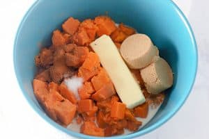 Cooked sweet potatoes, butter, brown sugar, cinnamon, and milk in a bowl, ready to be mixed.