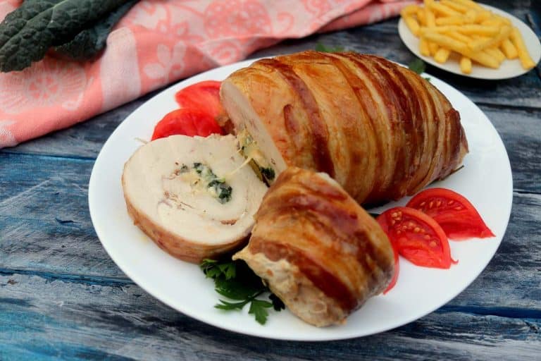Sliced stuffed turkey breast wrapped in crispy bacon, served with fresh tomato slices.