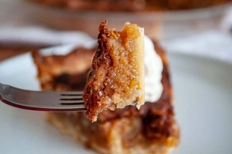 Close-up of a fork holding a bite of gooey pecan pie with a flaky crust.