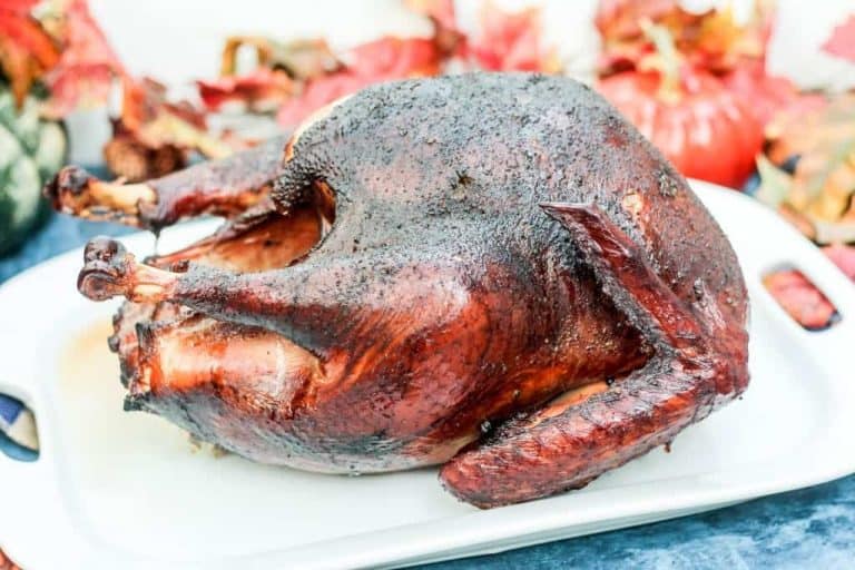 Whole pecan-smoked turkey with a dark, crispy skin on a white platter.