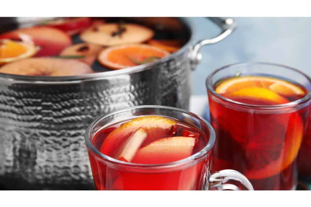 Warm mulled wine with orange slices and spices in glass mugs.