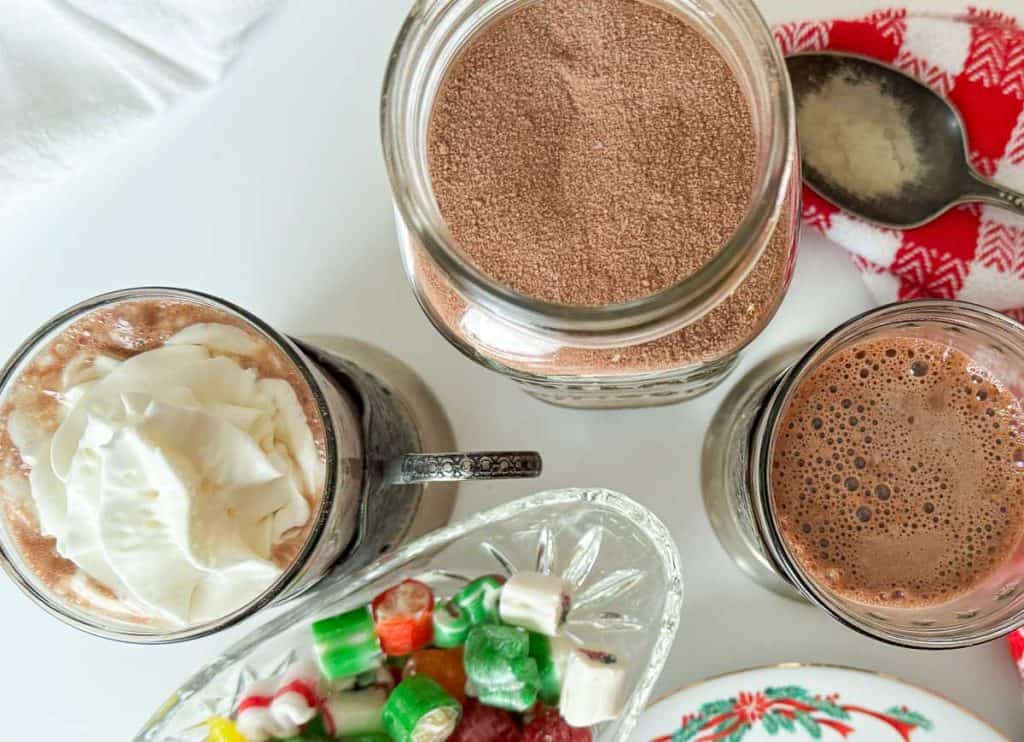 A jar of hot cocoa mix, a cup of cocoa, and christmas candy.