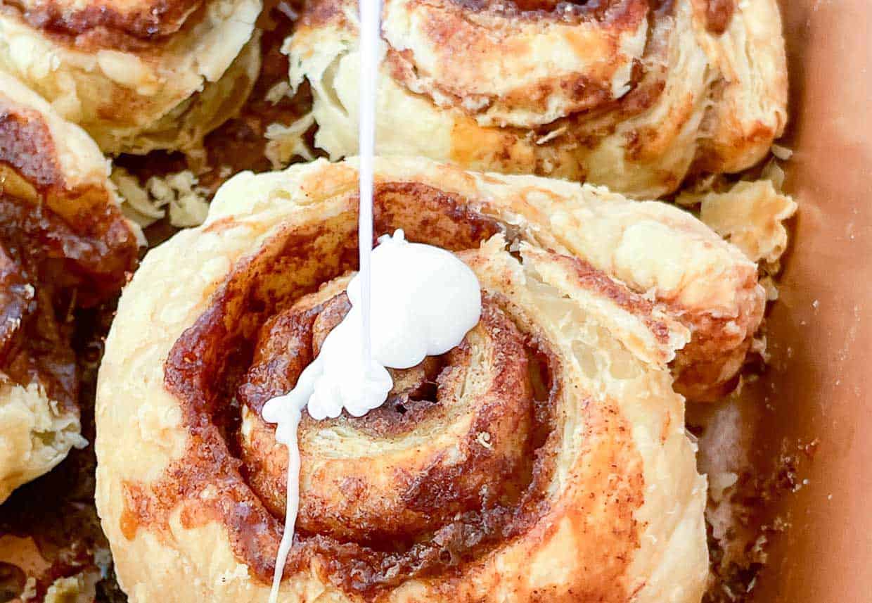 Frosting being drizzled on a crispy cinnamon roll.