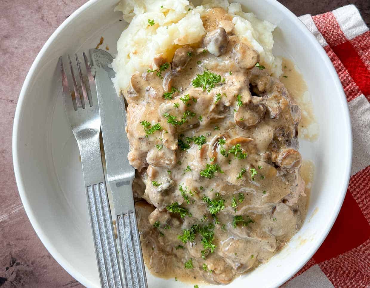 A bite of pork chops, mushrooms, and gravy on a fork.