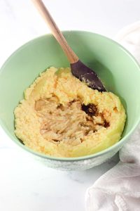 The same bowl with mashed bananas and vanilla added to the creamed mixture, being stirred with a wooden spatula.