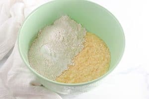 Dry ingredients, including flour, added to the wet batter in the bowl, ready to be mixed.