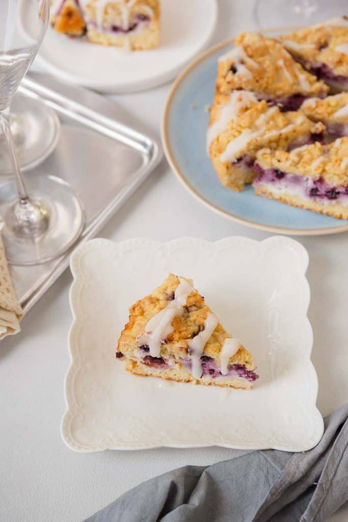 A piece of blueberry cheesecake crumb cake on a decorative white plate.