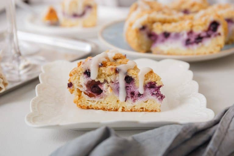 A close-up of a single slice of blueberry cheesecake crumb cake, showing the creamy cheesecake layer and juicy blueberries.