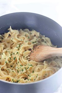 Buttered Noodles mixed with parsley in a pot with a wooden spoon.