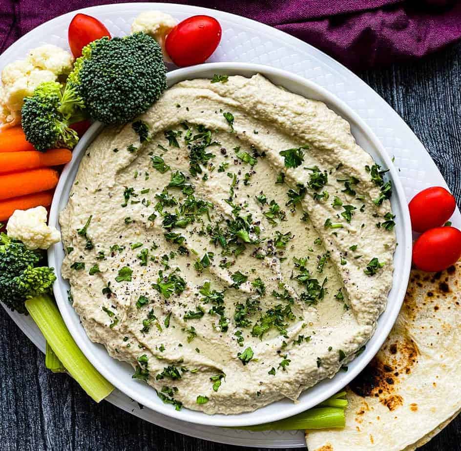Bowlog roasted eggplant baba ganoush dip with broccoli, cauliflower, carrots, cherry tomatos, and tortilla in a plate.