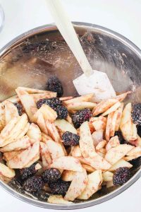 Mixed apple and blackberry filling with a spatula in the bowl.