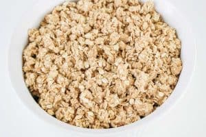 Unbaked crisp topping spread evenly over the fruit filling in a white baking dish.