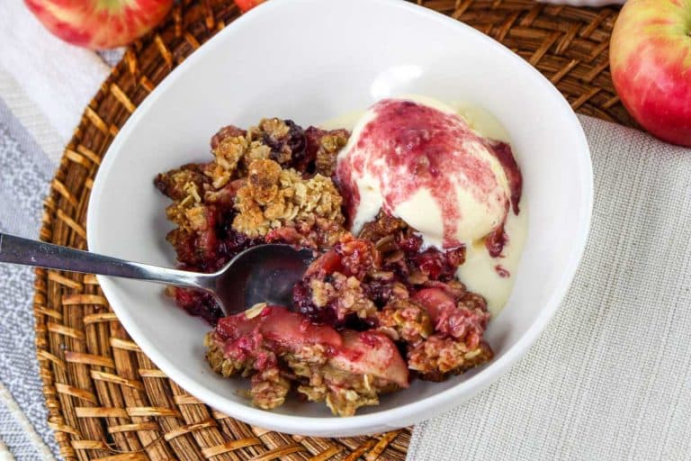A serving of Apple Blackberry Crisp in a white bowl with vanilla ice cream.
