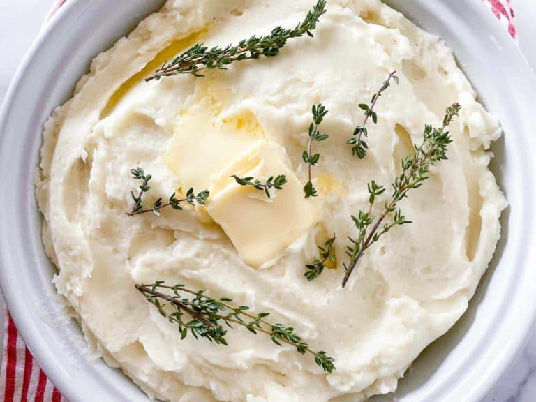 A bowl of creamy whipped potatoes topped with melting butter and fresh thyme sprigs.