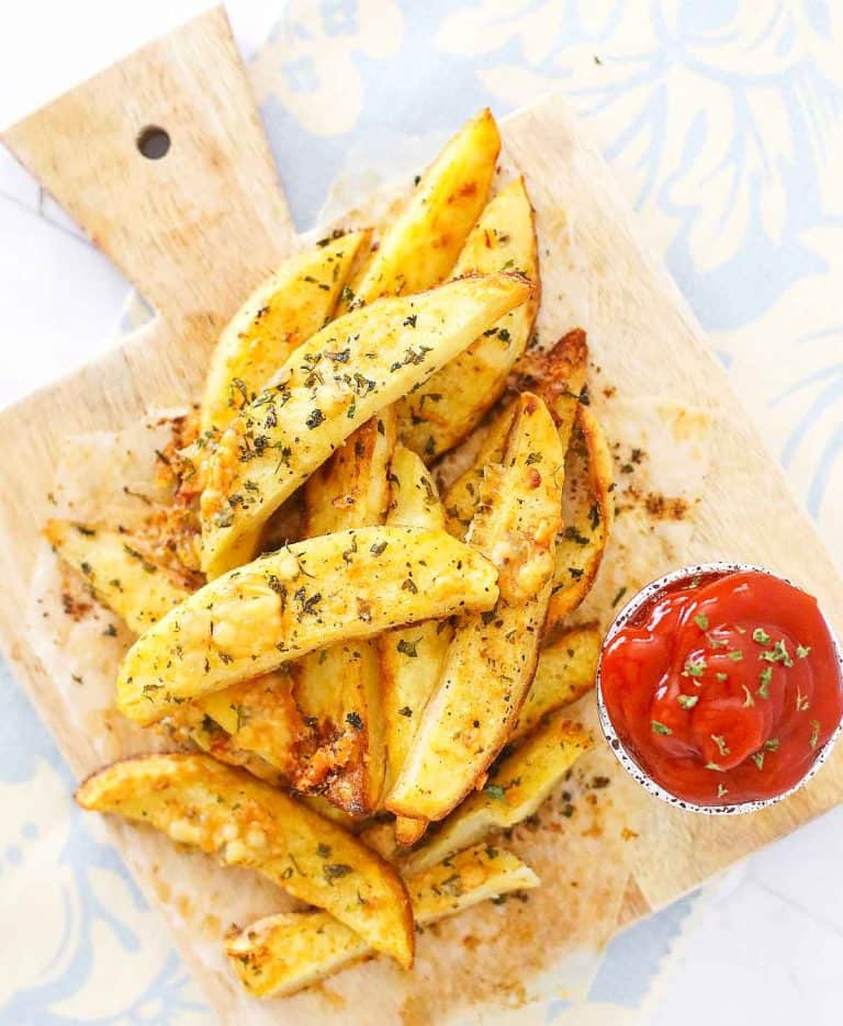 Crispy potato wedges on a wooden board with a cup of ketchup.