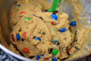 Cookie dough with M&M’s in a mixing bowl with a green spatula.