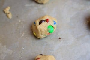 M&M cookie dough ball on a parchment-lined baking sheet.