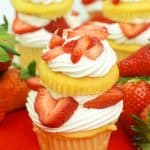 Multiple strawberry shortcake cupcakes on a red background.