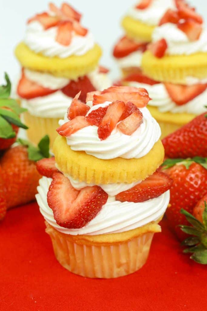 Multiple strawberry shortcake cupcakes on a red background.