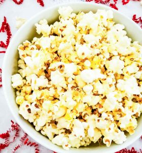 Overhead view of a bowl of popcorn on a white surface with red paper curls.