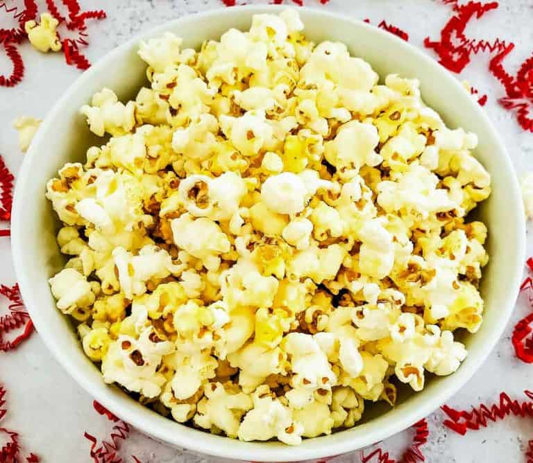 Overhead view of a bowl of popcorn on a white surface with red paper curls.