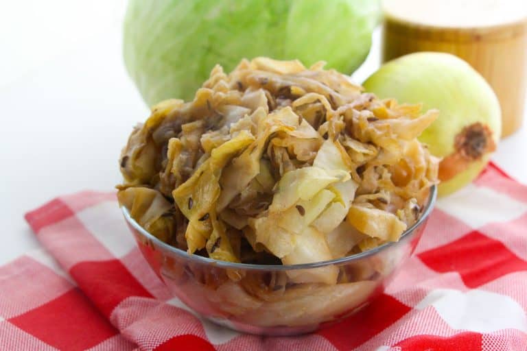 Close-up of braised cabbage in a glass bowl on a red-checked cloth.