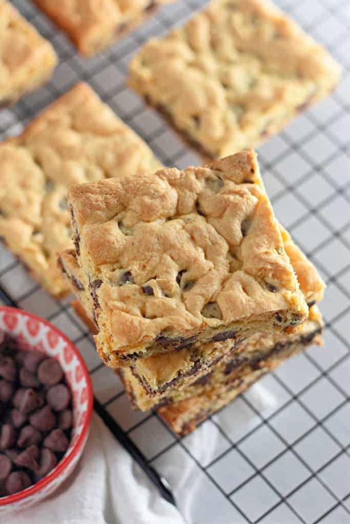 Overhead view of stacked cookie bars on a cooling rack beside a bowl of chips.