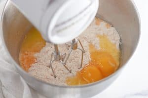 Electric mixer blending eggs and cake mix in a metal bowl.