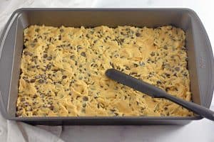 Cookie dough spread evenly in a metal baking pan.