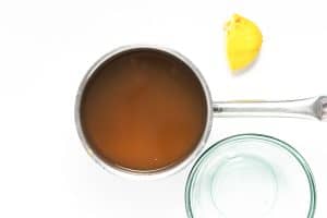Pot of amber-colored dandelion syrup with lemon peel and jar nearby.