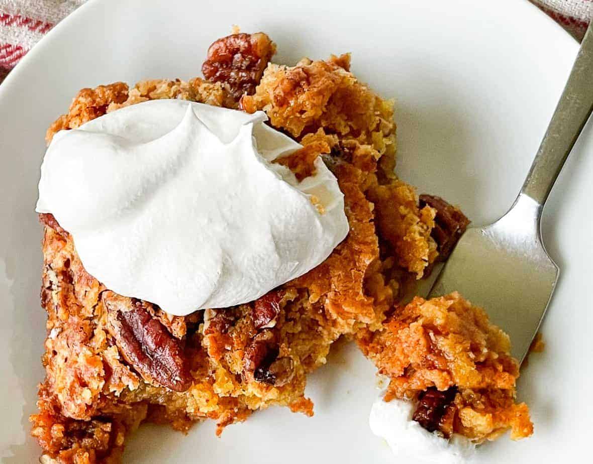 A bite of pumpkin crunch cake on a fork with a piece next to it with a dollop of whipping cream.
