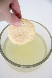 A hand dipping a baked cookie into the bowl of lemonade concentrate.