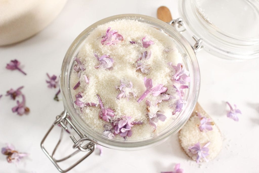 Close-up of a glass jar with lilac sugar, showing lilac petals mixed into the sugar.
