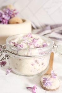 Close-up of a glass jar with lilac sugar, showing lilac petals mixed into the sugar.