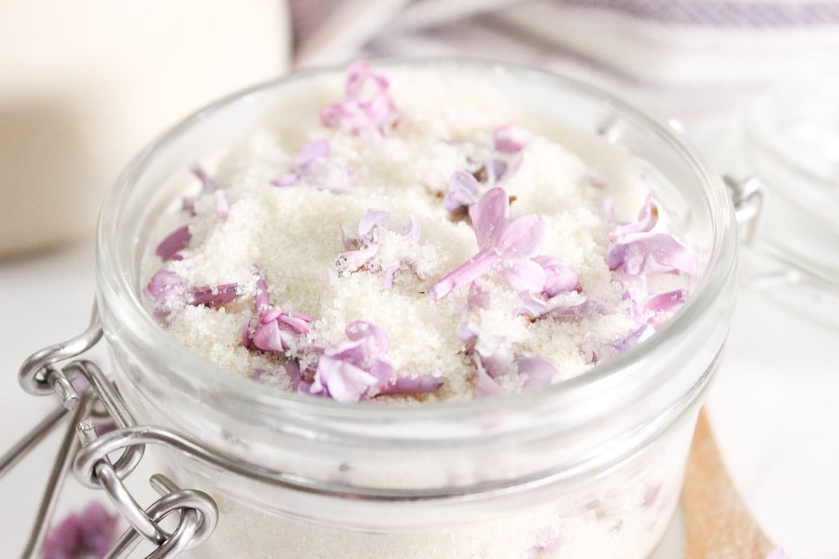Close-up of a glass jar with lilac sugar, showing lilac petals mixed into the sugar.