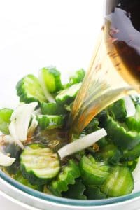 Pouring brine over sliced cucumbers and onions in a bowl.