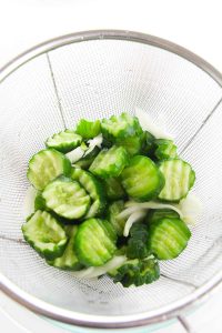 Cucumbers and onions drained in a mesh strainer.