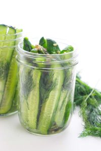 Two glass jars with sliced cucumbers, dill, and garlic on a white background.
