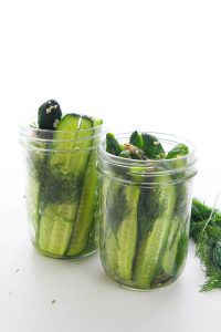 Close-up of glass jars with sliced cucumbers and dill.
